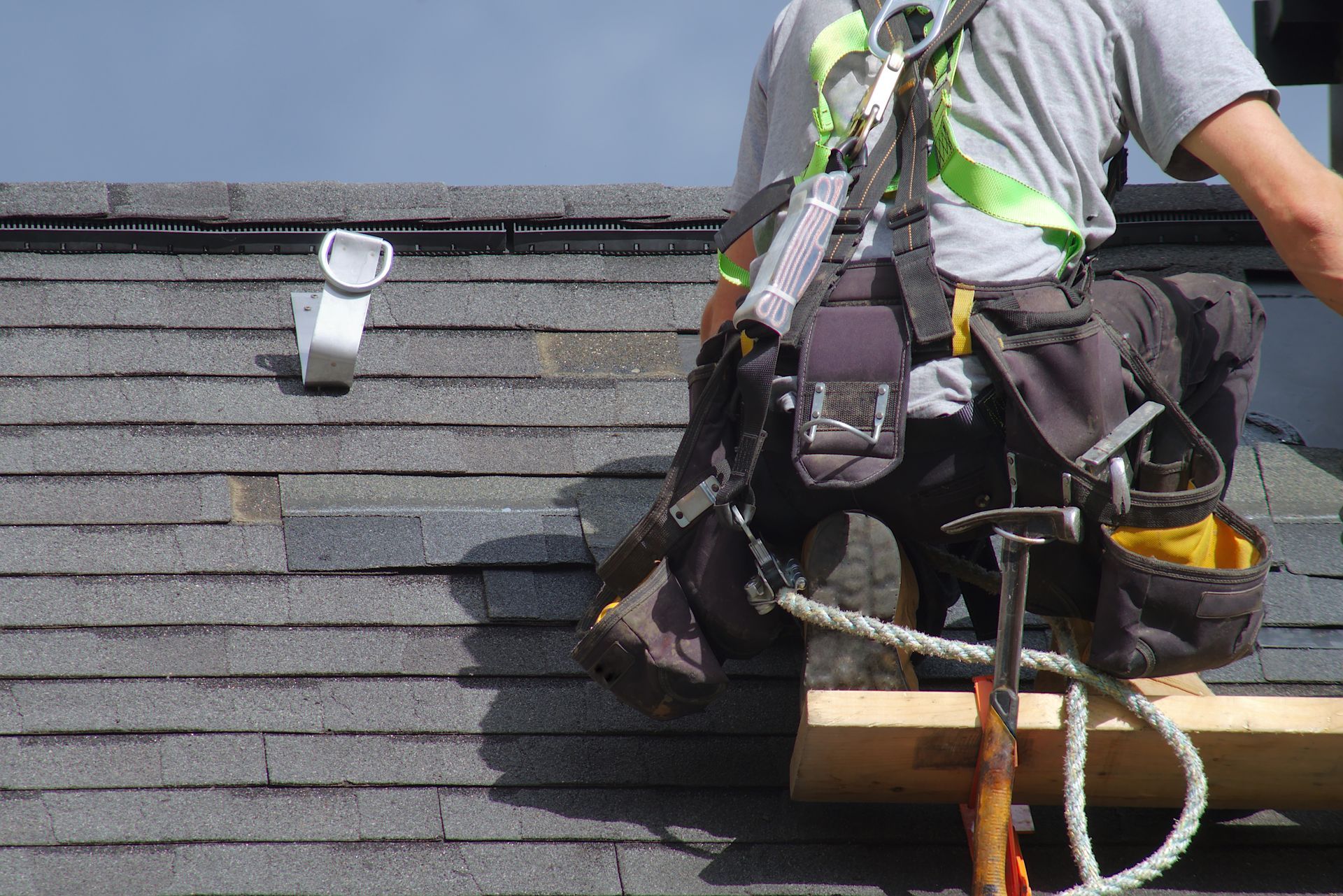 Ouvrier travaillant sur un toit en bardeaux, utilisant un harnais et des outils lors de la réparation du toit.