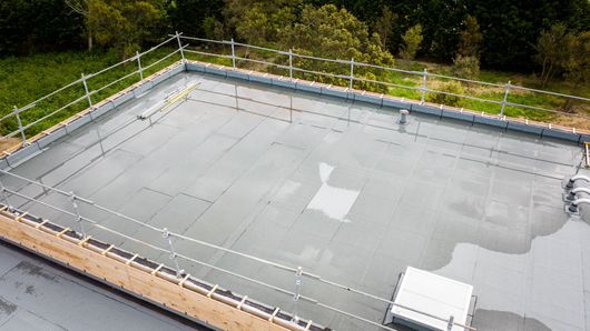 Toit recouvert d'une membrane d'étanchéité grise, bordé de rambardes de sécurité et d'arbres en arrière-plan.
