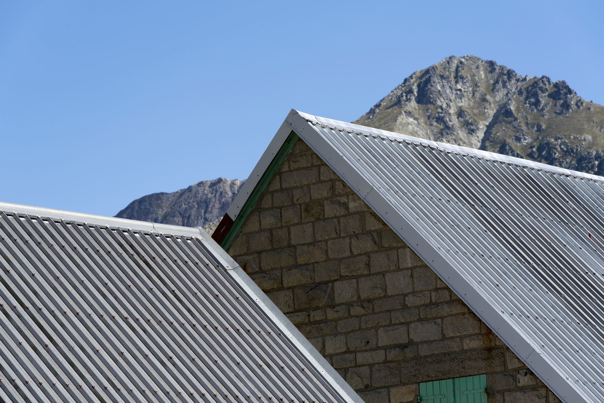 Toits en tôle ondulée devant une montagne rocheuse sous un ciel bleu clair.