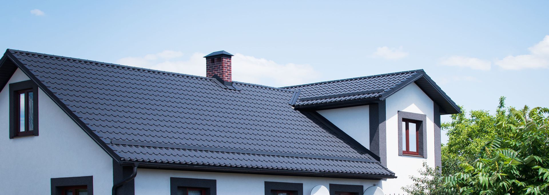 Maison blanche au toit gris foncé et à la cheminée rouge sous un ciel dégagé.