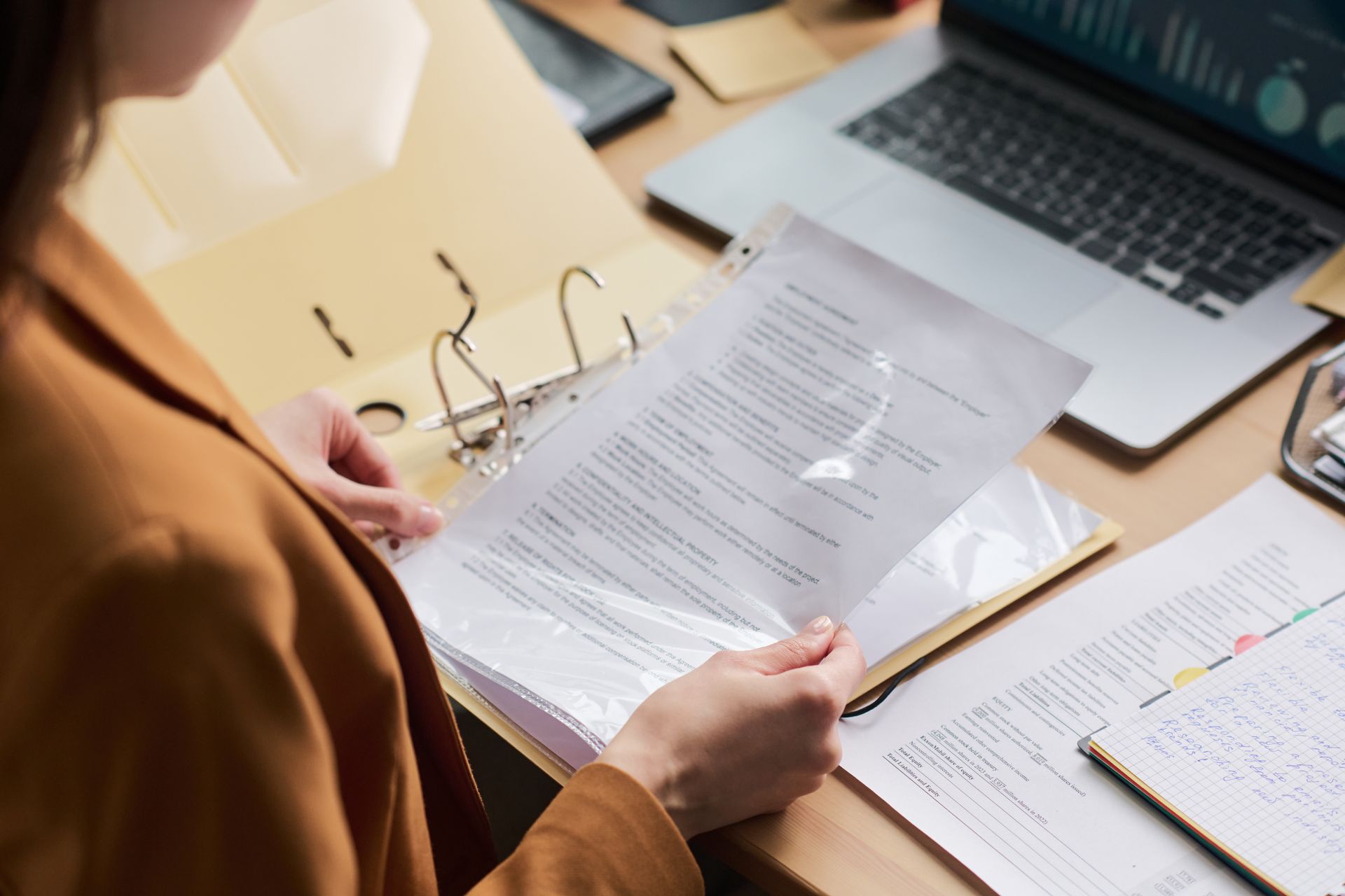Une personne corrigeant des articles, assise à un bureau avec un ordinateur portable et un cahier.