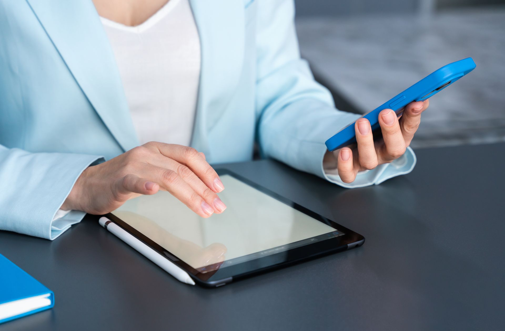 Une personne utilisant une tablette et tenant un smartphone bleu à un bureau.