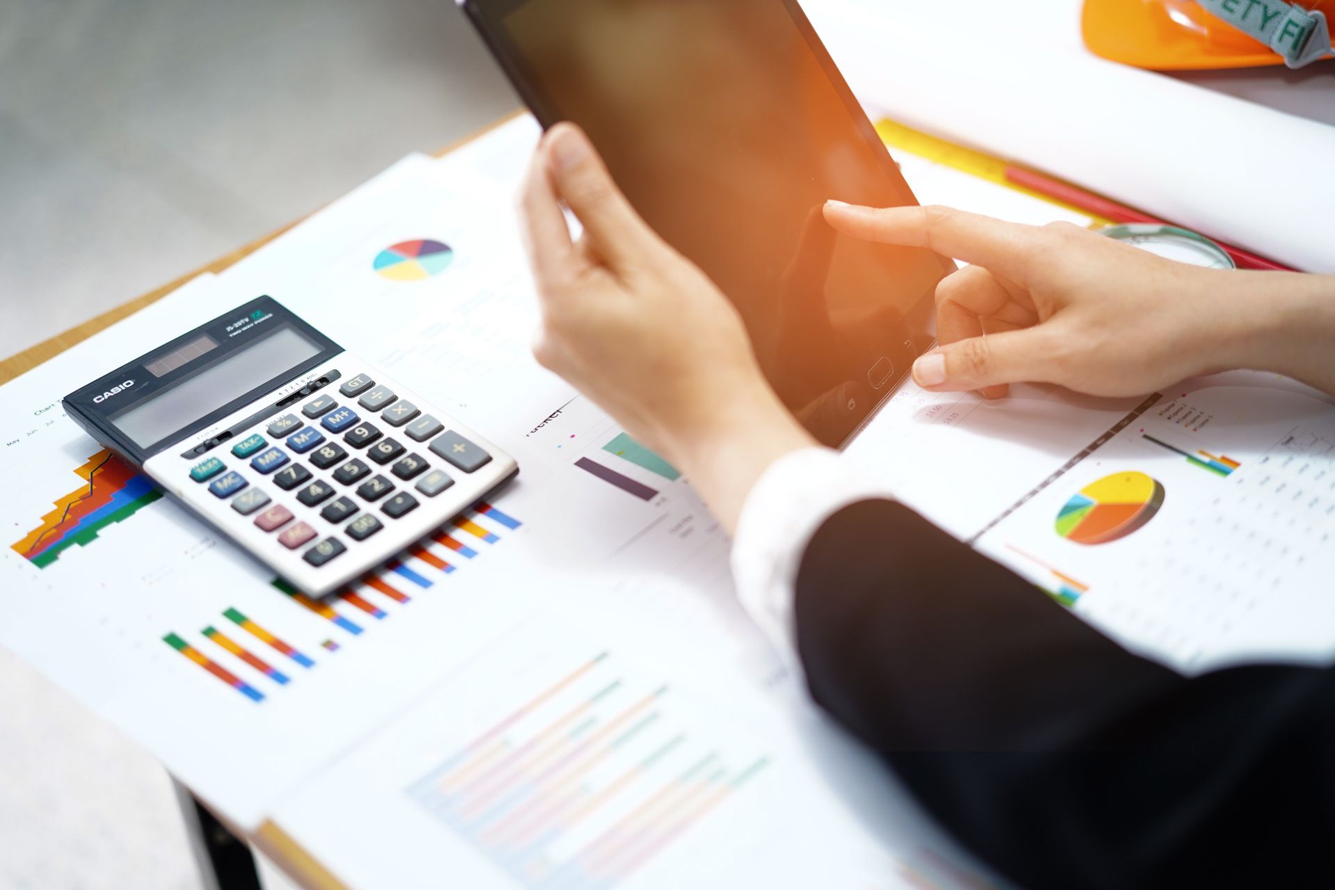 Des mains manipulant une calculatrice au-dessus de graphiques et de documents financiers posés sur un bureau.