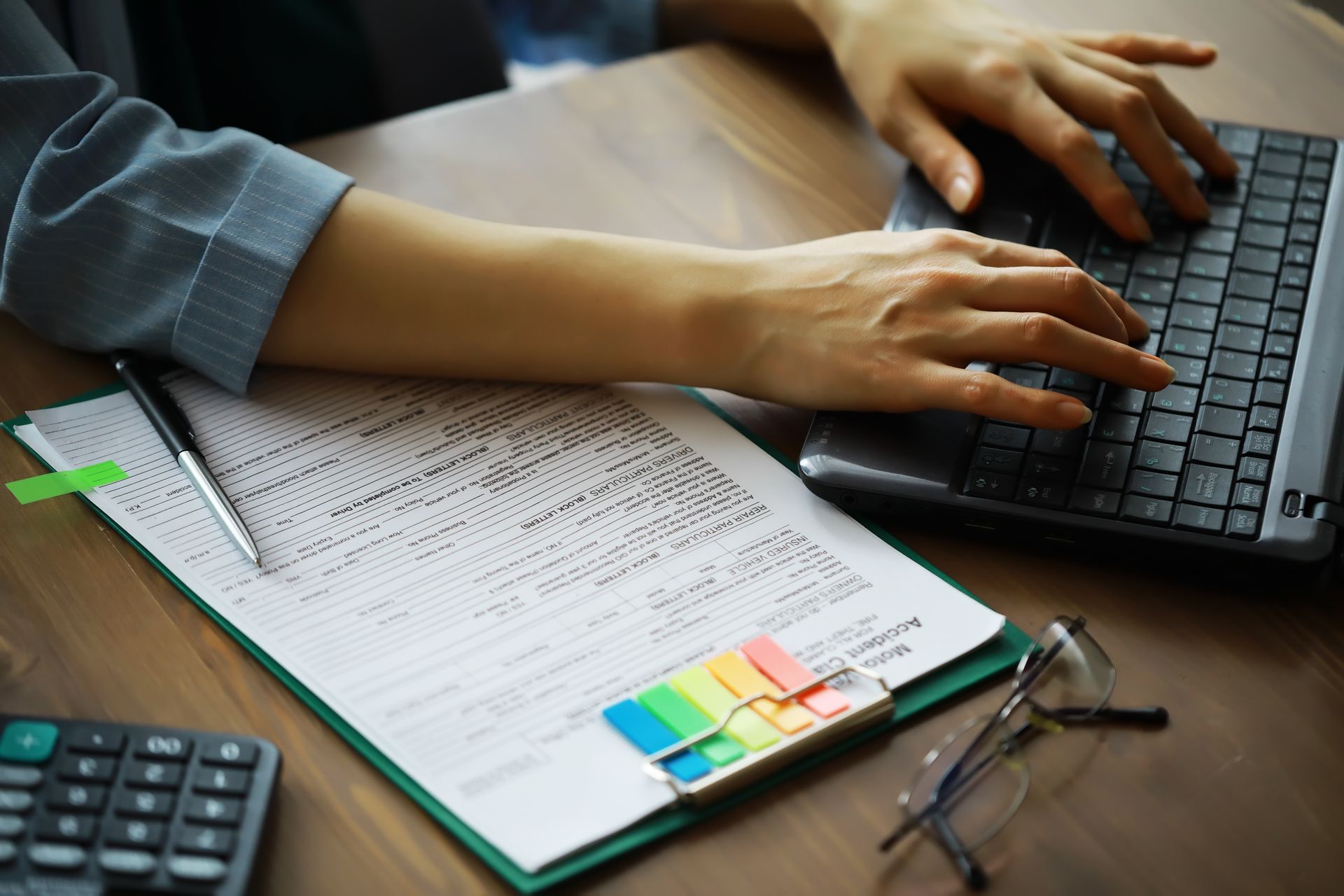 Des mains tapant sur un ordinateur portable à côté d'un bloc-notes avec des papiers et des post-it colorés sur un bureau.