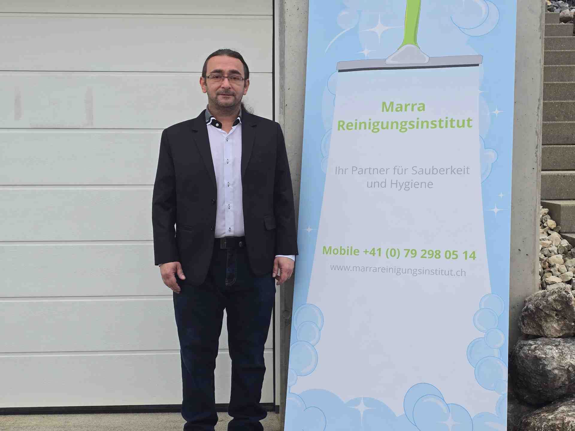 Eine Person putzt mit einem Abzieher ein Fenster auf einer Leiter. Unten auf der Terrasse steht ein roter Eimer.