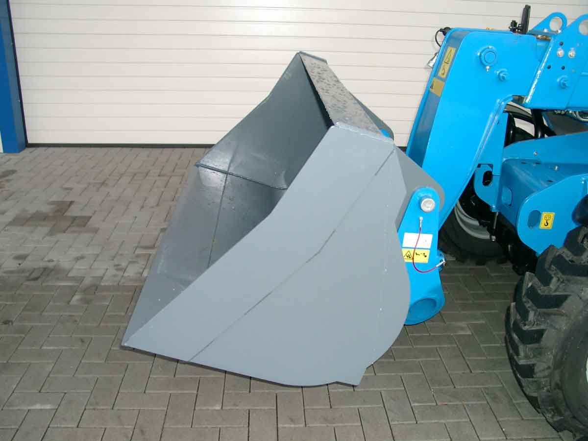Graue Baggerschaufel an einem blauen Traktor, der auf einer befestigten Fläche parkt.