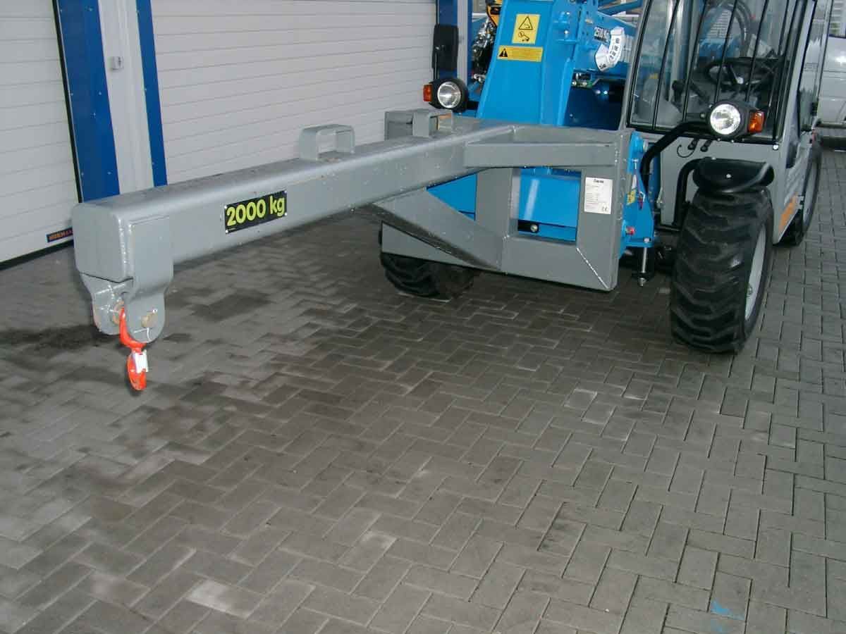 Grauer Traktor mit ausgefahrenem Gabelstaplerarm parkt auf einer gepflasterten Fläche neben einem blauen Garagentor.