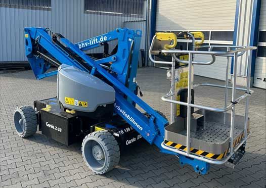 Eine blaue Genie-Hebebühne mit grauer Arbeitsbühne steht auf einem gepflasterten Parkplatz in der Nähe eines Gebäudes.