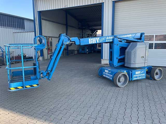 Blaue Hubarbeitsbühne mit ausgefahrenem Arm, geparkt vor einer Laderampe eines Lagerhauses
