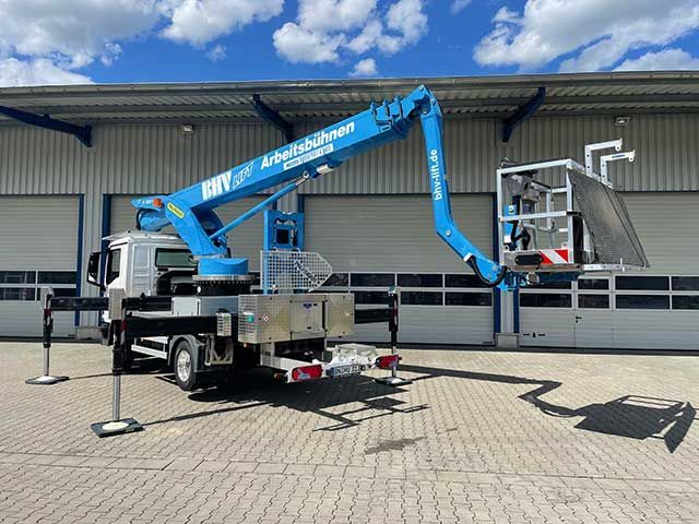 Blauer Hubarbeitsbühnenwagen mit ausgefahrenem Arm neben einem Industriegebäude unter einem teilweise bewölkten Himmel