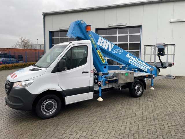 Ein weißer Lieferwagen mit blauer Hubarbeitsbühne parkt vor einem Lagerhaus auf einem gepflasterten Parkplatz.