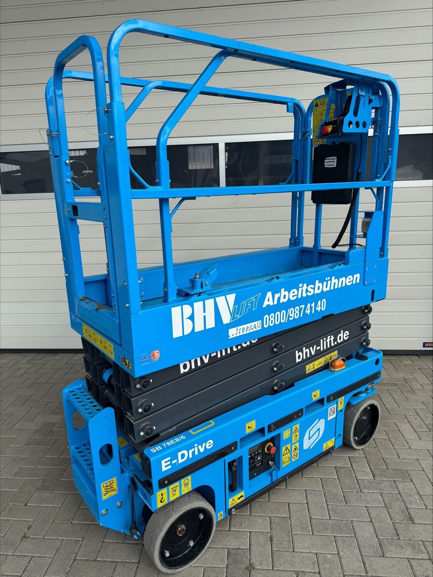 Eine Reihe blauer Scheren- und Hubarbeitsbühnen steht an einem bewölkten Tag im Freien.