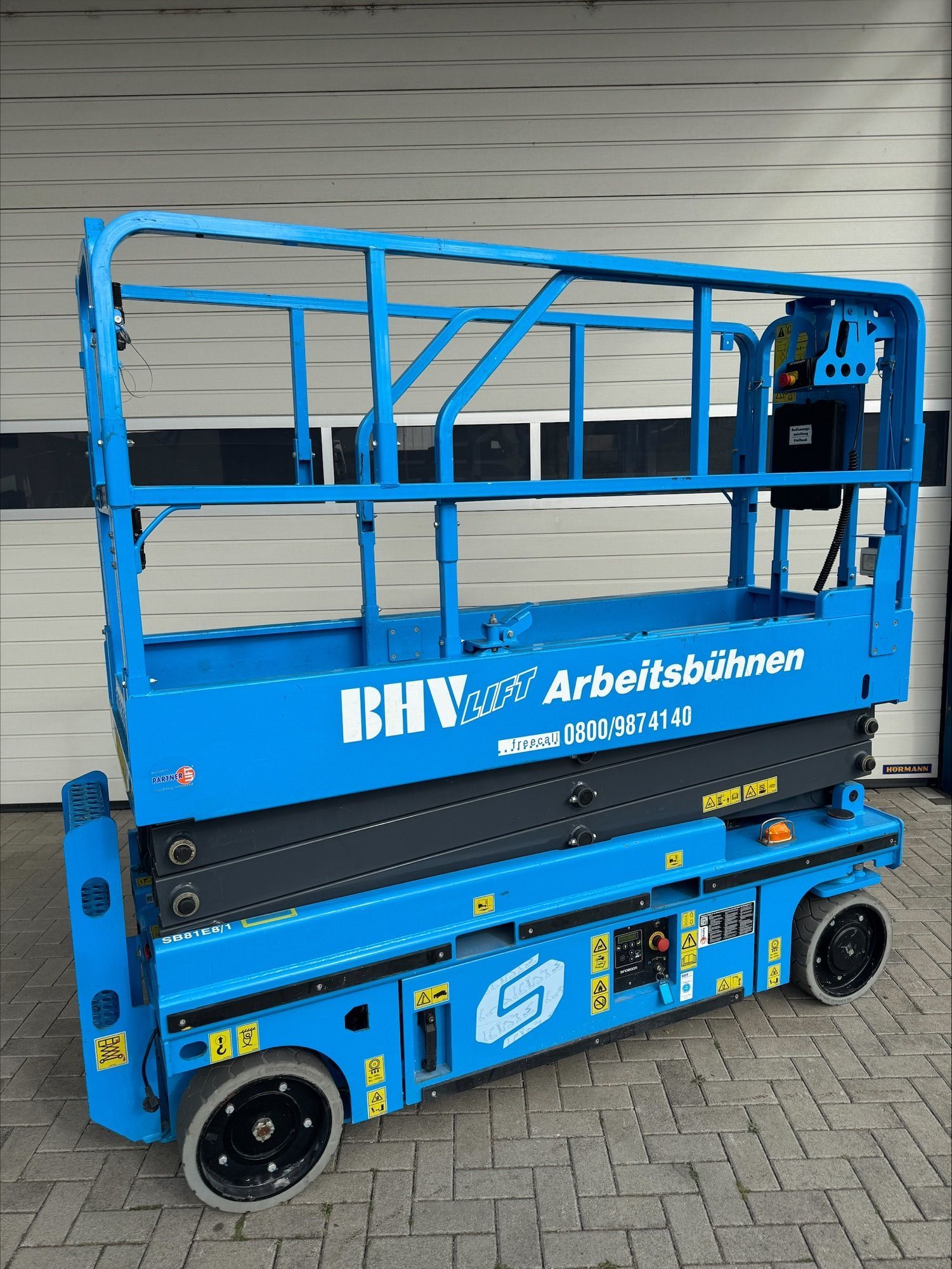 Eine Reihe blauer Scheren- und Hubarbeitsbühnen steht an einem bewölkten Tag im Freien.