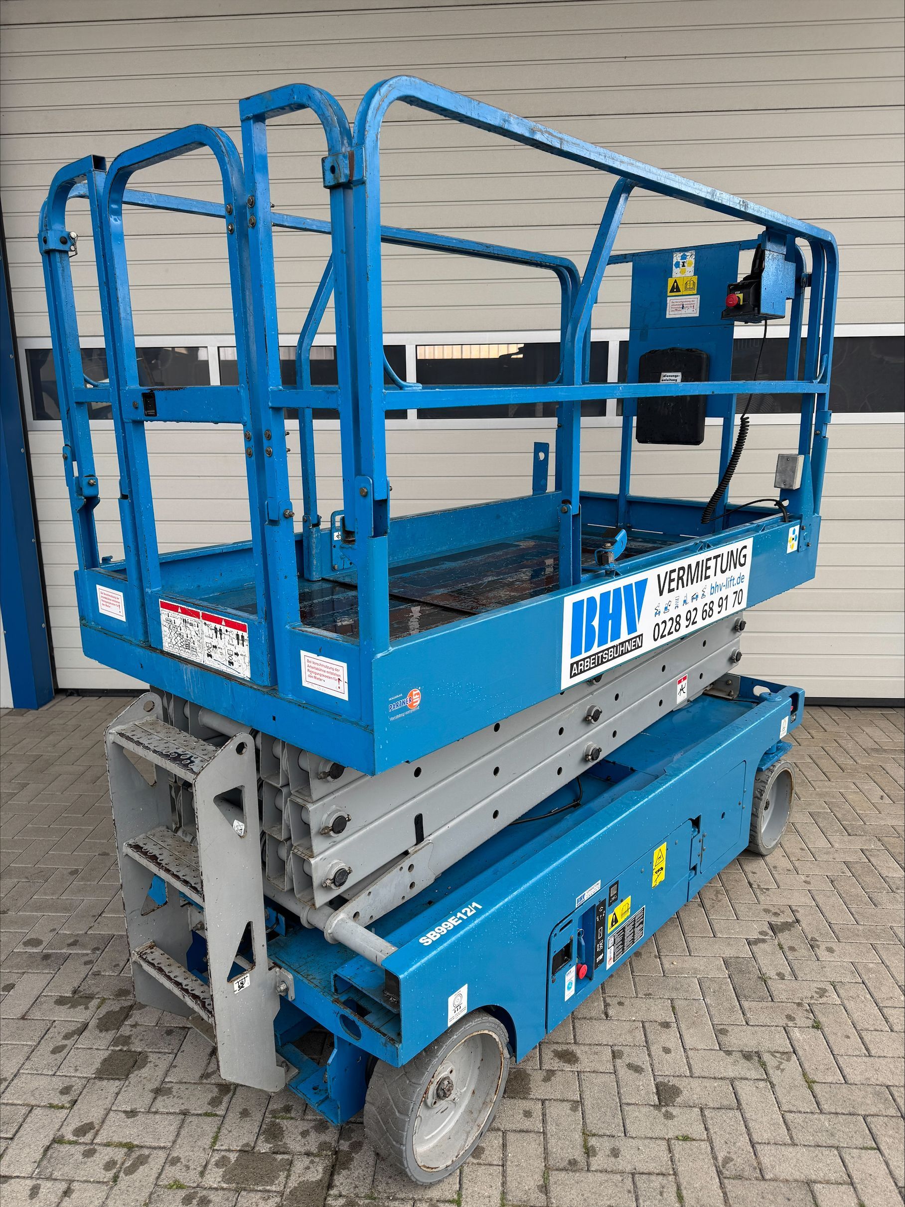 Eine Reihe blauer Scheren- und Hubarbeitsbühnen steht an einem bewölkten Tag im Freien.