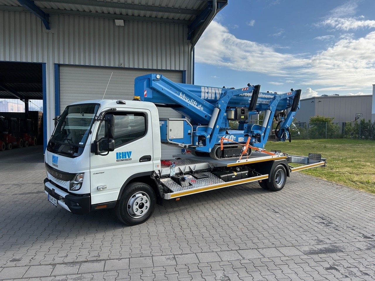 Ein weißer Servicewagen mit blauer Hubarbeitsbühne parkt neben einer Laderampe in einem Lagerhaus.