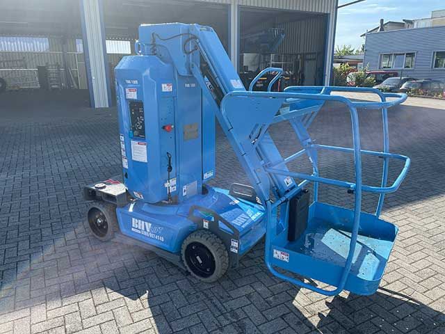 Eine blaue Hubarbeitsbühne steht auf einem gepflasterten Parkplatz vor einem Industriegebäude.
