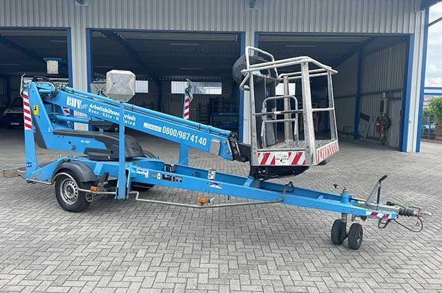Eine blaue, auf einem Anhänger montierte Hubarbeitsbühne mit ausgefahrenem Ausleger und Arbeitskorb