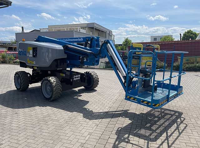 Blaue Hubarbeitsbühne mit erhöhter Plattform, die im Freien auf einem gepflasterten Parkplatz abgestellt ist.