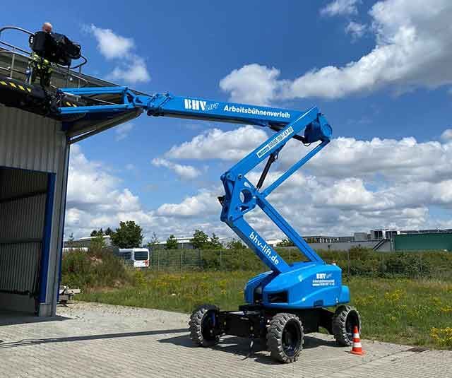 Blaue Hubarbeitsbühne mit einem Arbeiter, der neben einem Gebäude unter einem teilweise bewölkten Himmel hochgezogen wurde.