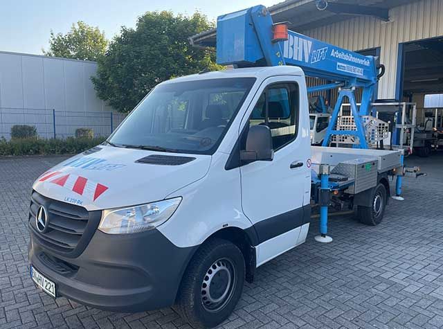 Weißer Lieferwagen mit blauer Hubarbeitsbühne parkt vor einer Werkstatt
