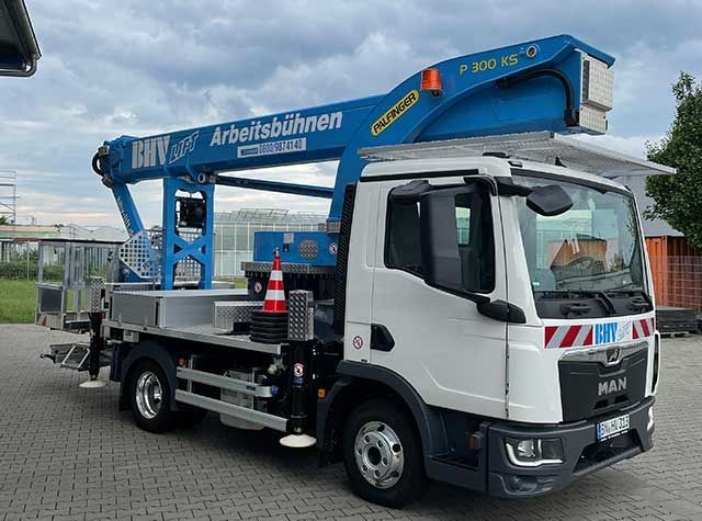 Ein blau-weißer, auf einem Lkw montierter Hubsteiger steht im Freien unter bewölktem Himmel.