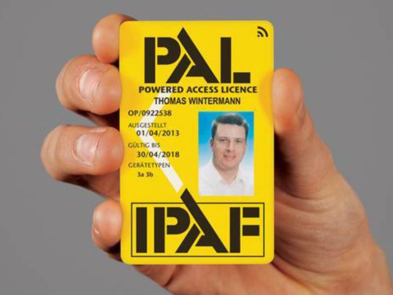 In der Hand wird eine gelbe PAL IPAF-Zugangslizenzkarte mit einem kleinen Porträtfoto gehalten.