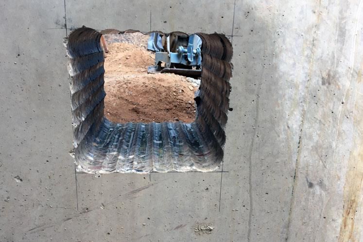 Ein Loch in einer Betonwand mit einem Bild eines Bulldozers im Hintergrund