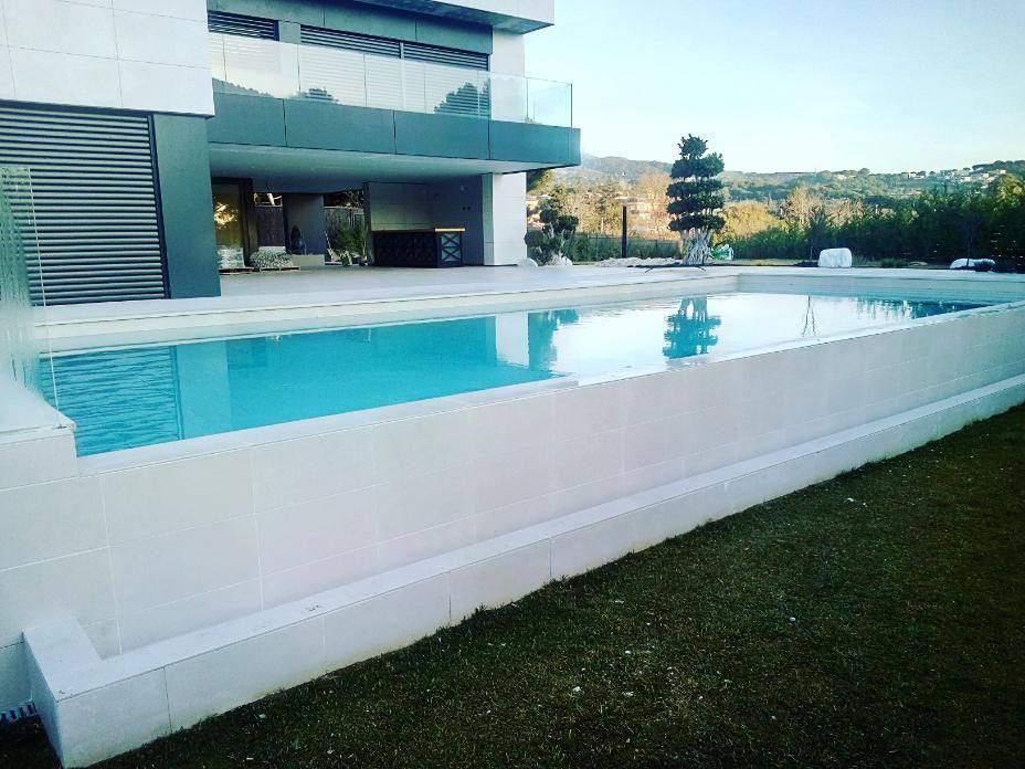 Una piscina rectangular de paredes blancas y agua turquesa frente a una casa moderna.