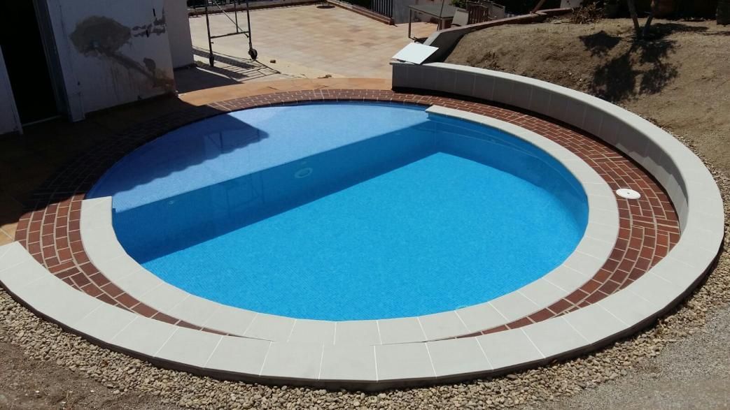 Piscina redonda azul con borde de ladrillo y hormigón. Exterior, en un entorno soleado.