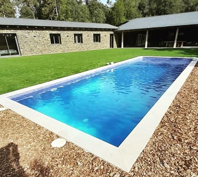 Piscina rectangular de agua azul junto a césped y edificio de piedra.