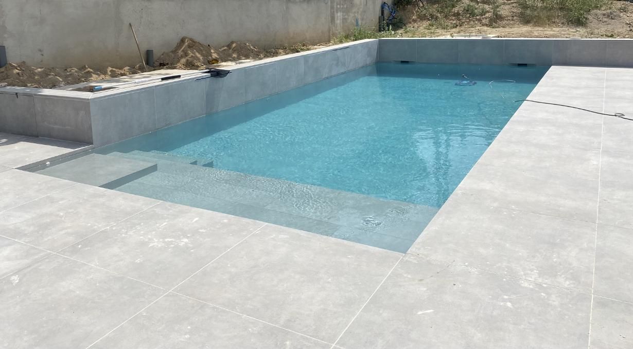 Piscina rectangular de agua azul claro y escalones, rodeada de azulejos grises y paredes de concreto.