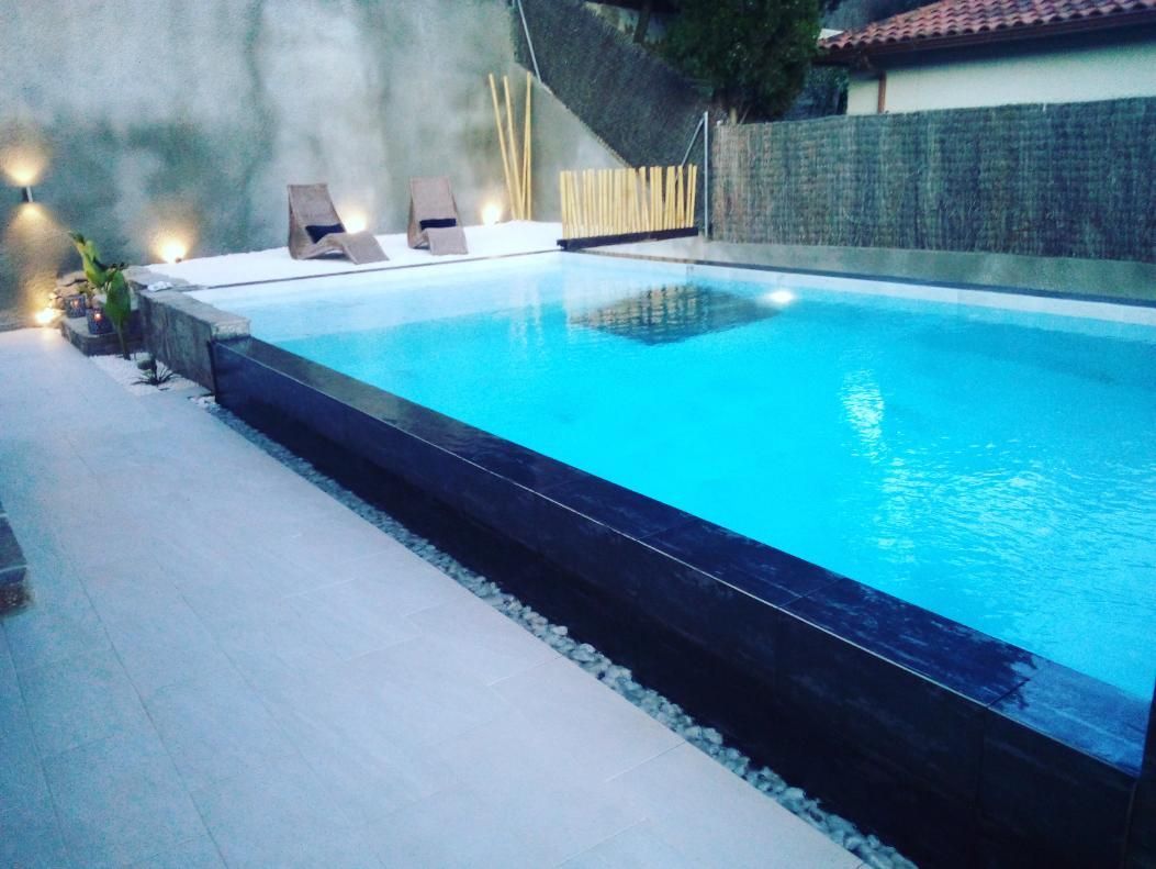 Piscina al atardecer con agua iluminada, camastros e iluminación decorativa.