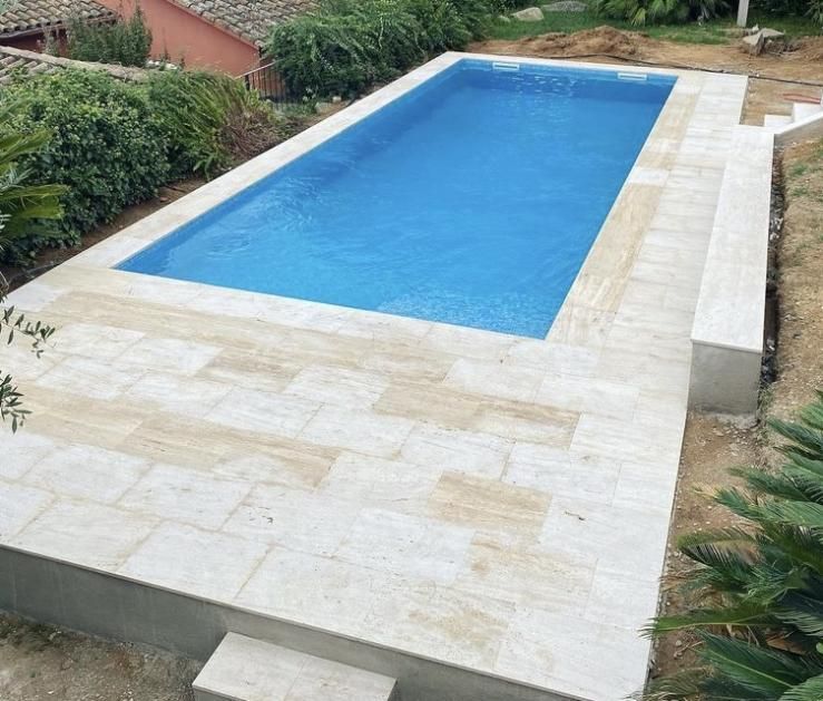 Piscina rectangular de agua azul, rodeada de piedra de color claro, pequeños escalones a un lado.