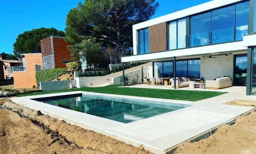 Casa moderna con piscina rectangular, asientos al aire libre y exuberante césped verde.