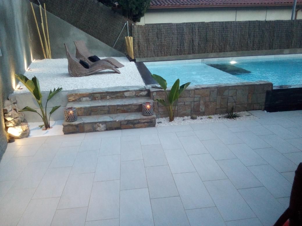 Patio de piedra con piscina, camastros y escalones, iluminado por la noche.