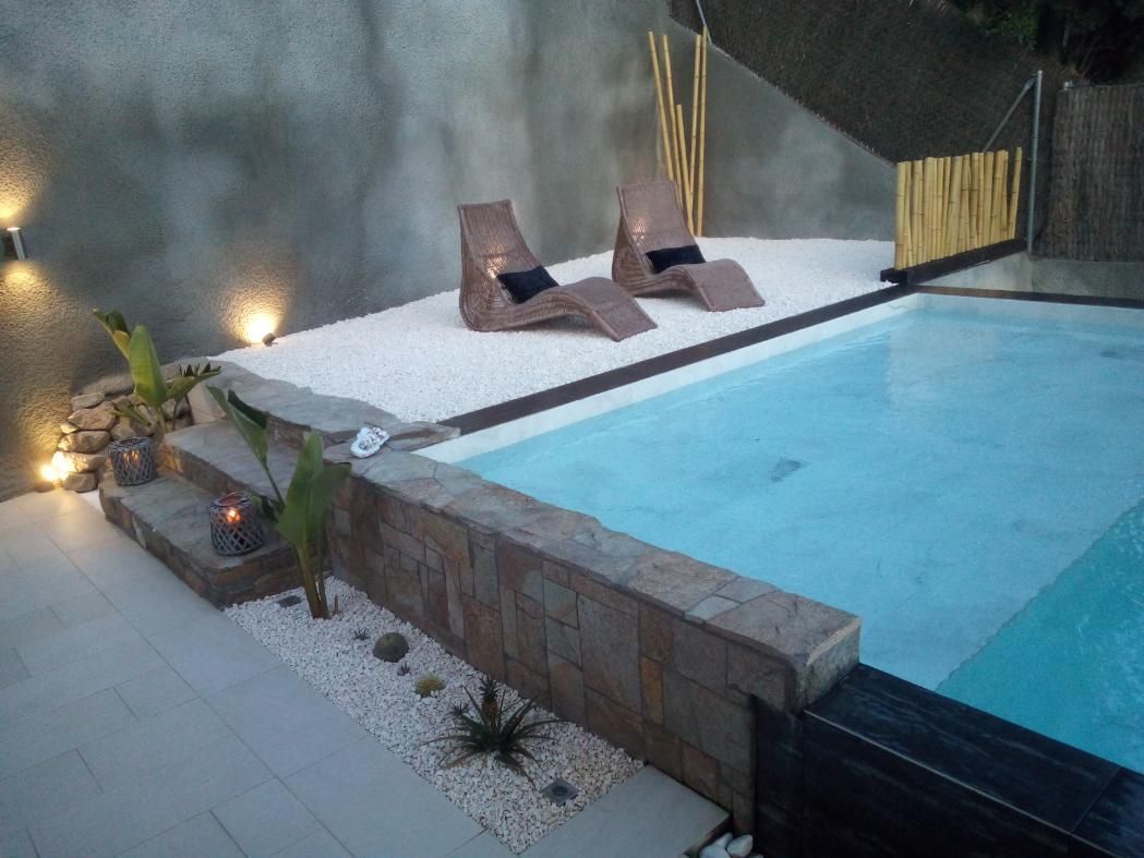 Piscina con tumbonas en una terraza blanca, pared de piedra y detalles de bambú.