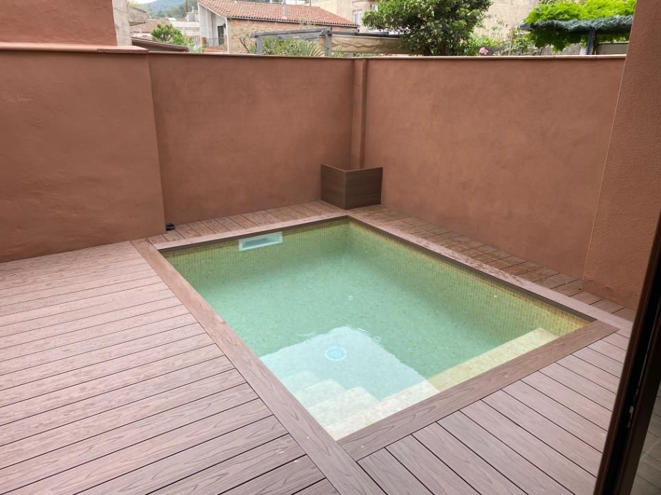 Pequeña piscina rectangular rodeada de tarima compuesta, frente a paredes de color marrón rojizo.