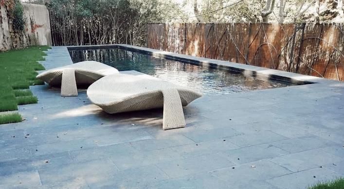 Dos modernas tumbonas junto a una piscina rectangular en un entorno de patio.