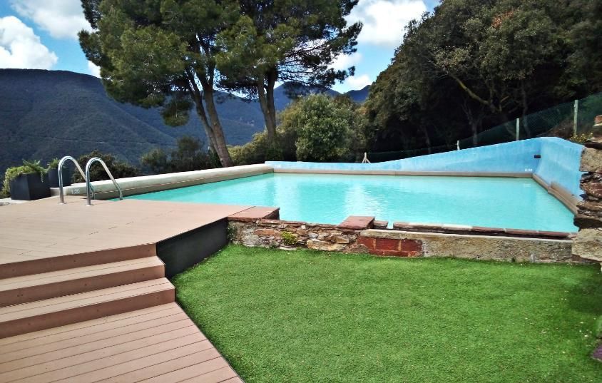 Piscina de agua turquesa rodeada de césped y terraza, con las montañas como telón de fondo.