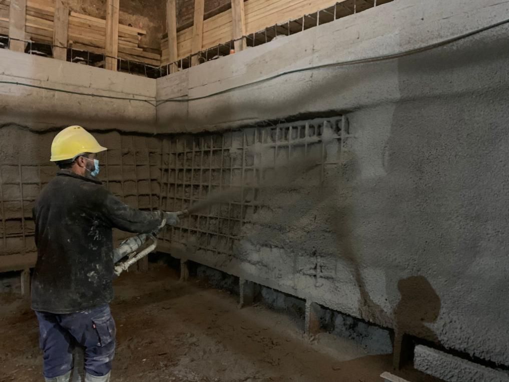 Trabajador con equipo de protección rociando hormigón sobre una pared en un sitio de construcción.