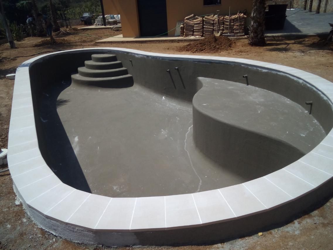 Piscina de nueva construcción con escalones, banco y borde blanco.