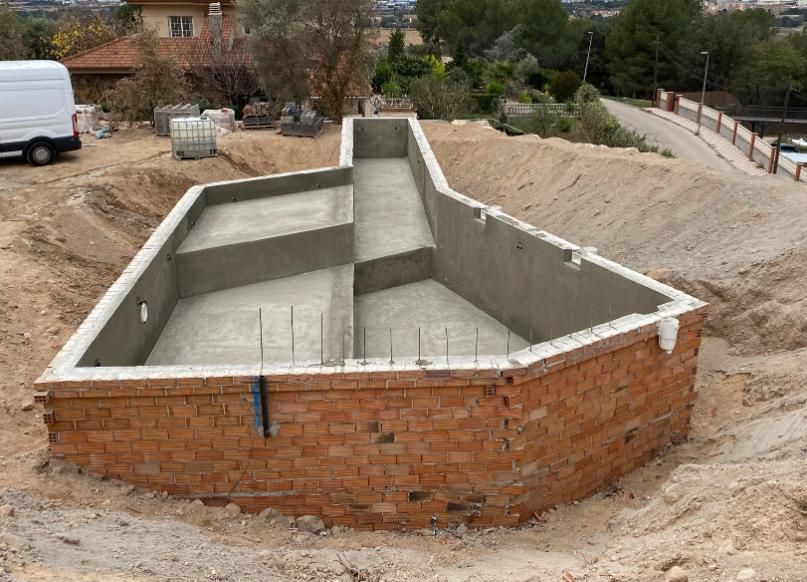 Una piscina parcialmente construida con paredes de ladrillo, interior de hormigón y tierra circundante.