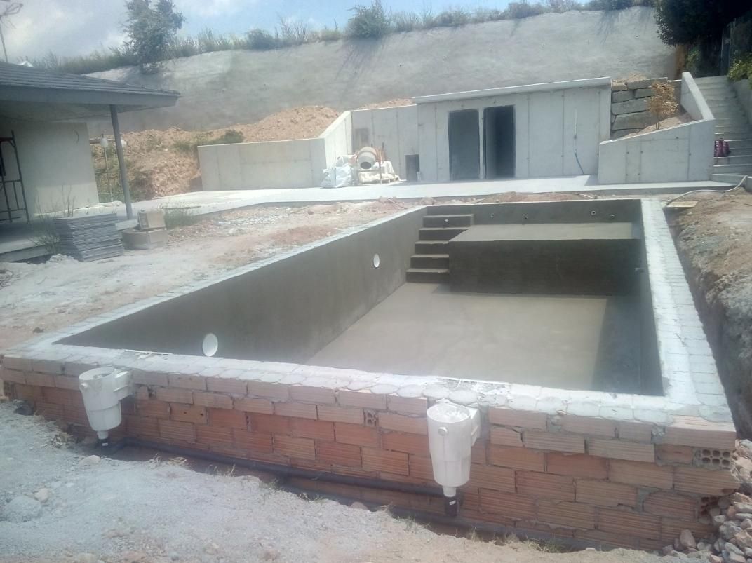 Construcción de una piscina rectangular con mampostería en un patio, al fondo se ve un edificio y una ladera.