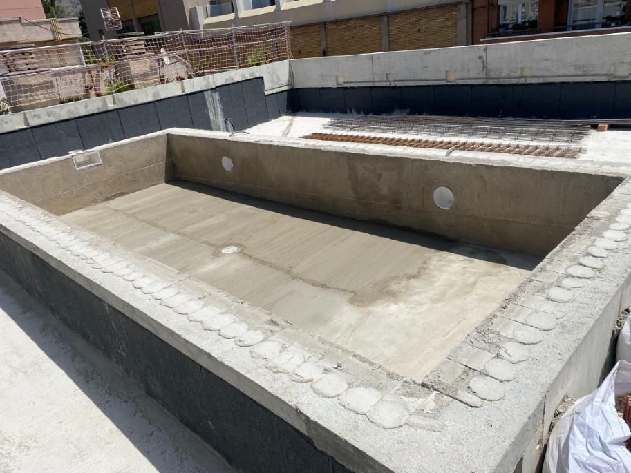 Construcción de una piscina rectangular de concreto, mostrando el interior y la estructura circundante; día gris y soleado.