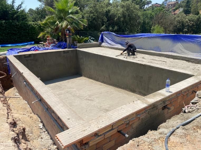 Construcción de una piscina rectangular: albañil trabajando en el interior, paredes grises, borde de ladrillo