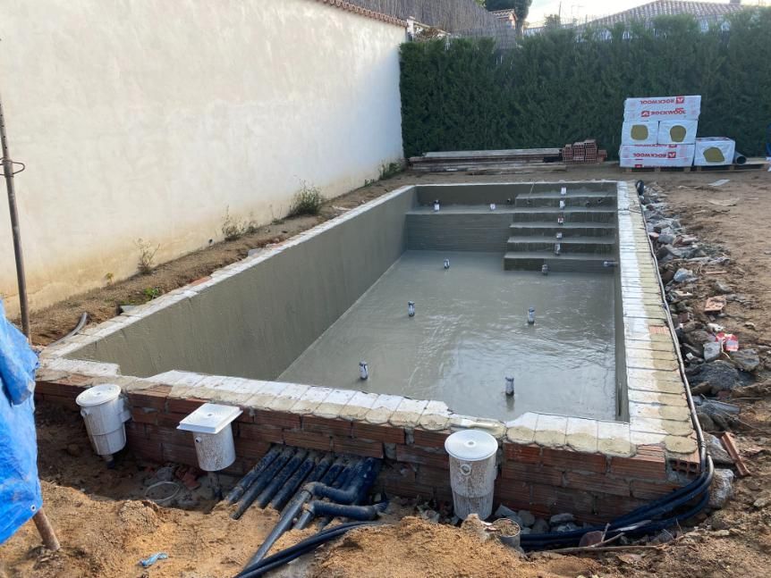 Piscina en construcción con paredes y escalones de hormigón, rodeada de obra vista y fontanería.
