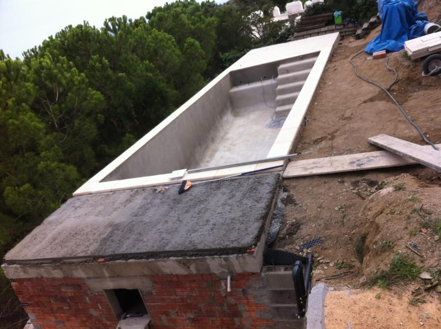Construcción de una piscina rectangular en ladera con muros y gradas de concreto, rodeada de tierra y árboles.