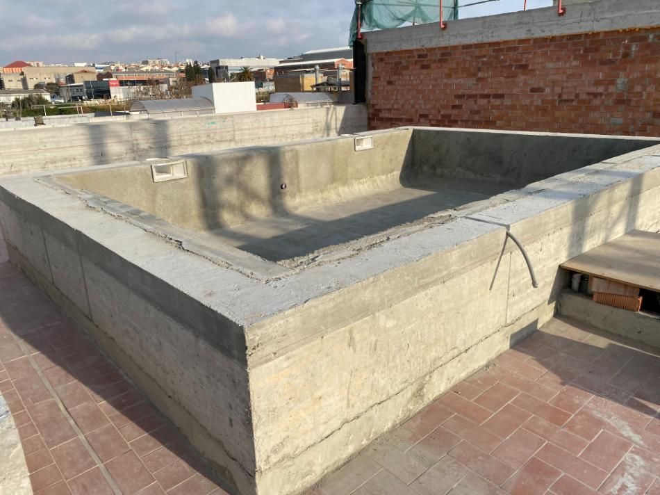 Piscina rectangular de hormigón en construcción sobre una azotea con estructuras de ladrillo al fondo.