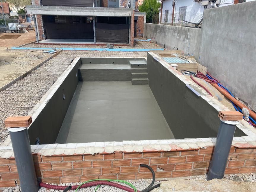 Piscina de hormigón en construcción, enmarcada por ladrillo y adyacente a un edificio.