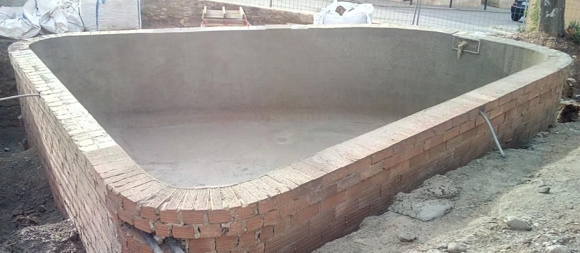 Piscina triangular de ladrillo vacía en construcción. Las paredes interiores son grises y lisas.